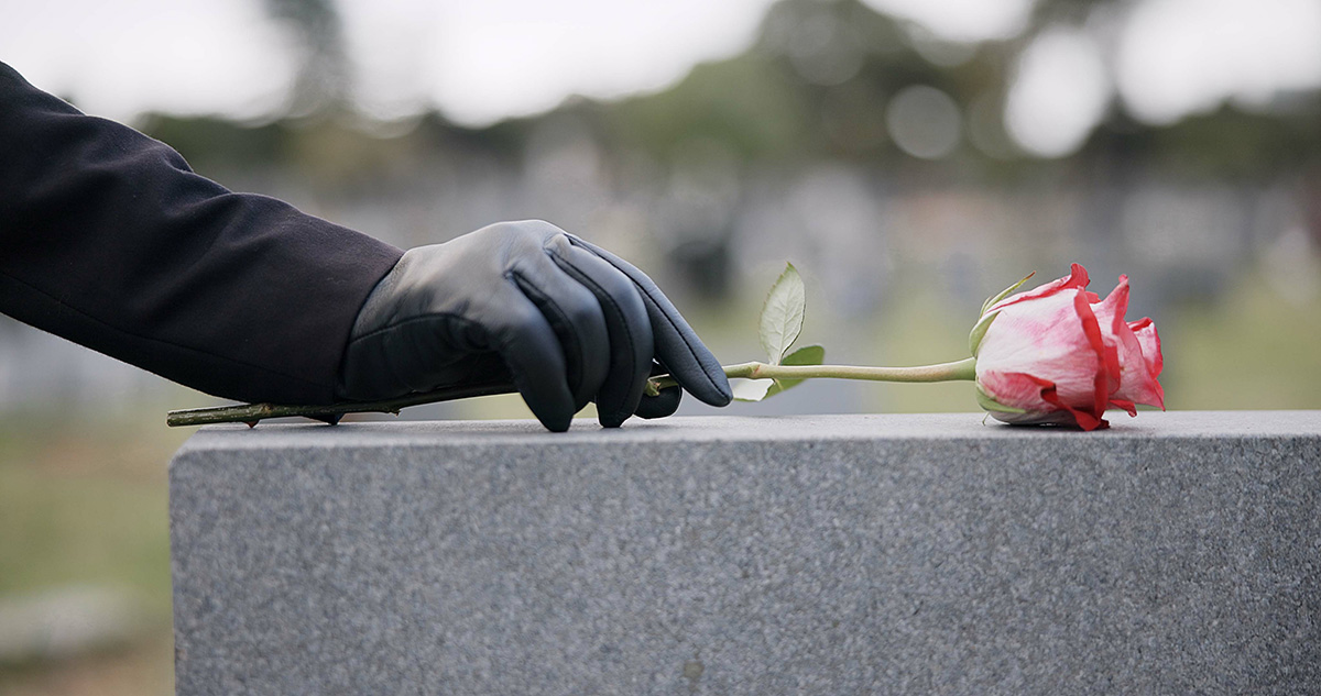 gloved-hand-placing-rose-on-a-tombstone-2026-03-25-01-35-14-utc
